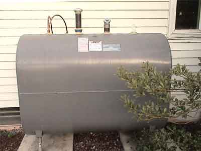 Above-ground oil tank installation - photo of gray oil tank installed above-ground in yard outside home.