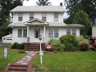 Photo of white two-story home with red brick steps and paver walkway with "For Sale" sign in front; Statewide Environmental Services LLC services the real estate industry.